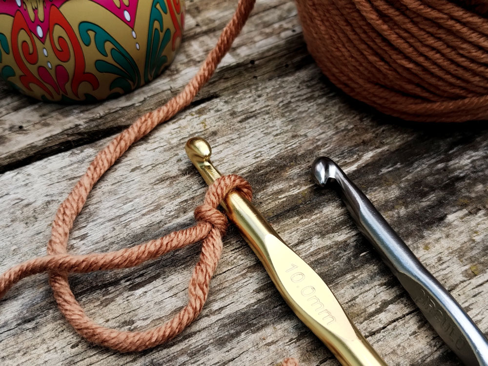 Yarn cake and crochet hook with a slip knot over a wooden surface.